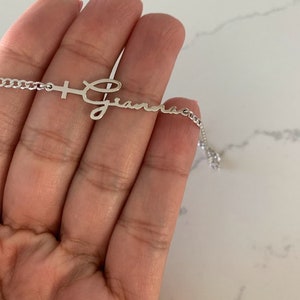 Puede incluir: Un collar de plata con una cruz y el nombre "Gianna" escrito en cursiva.