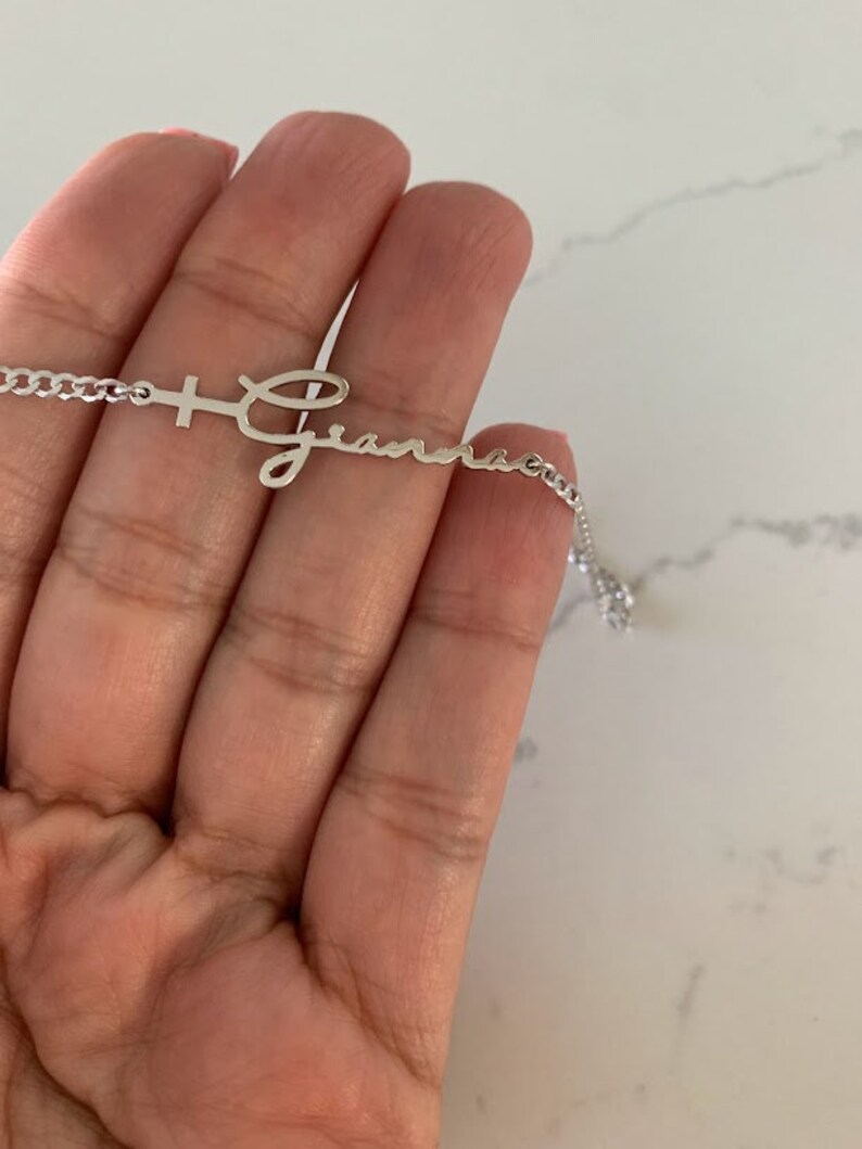 Puede incluir: Un collar de plata con una cruz y el nombre "Gianna" escrito en cursiva.
