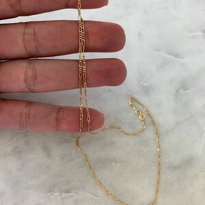 May include: A gold chain necklace with a delicate, figaro chain design. The chain is approximately 18 inches long.