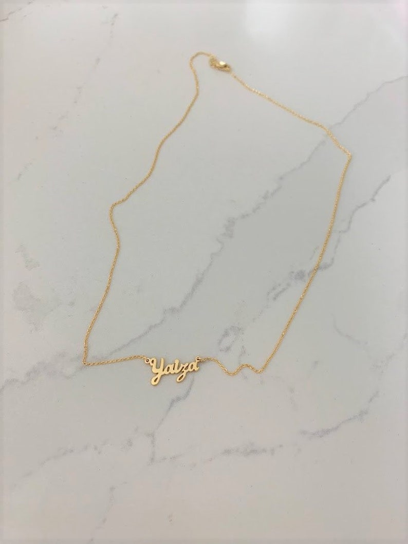 May include: A gold chain necklace with a cursive name pendant that reads "Yalza".