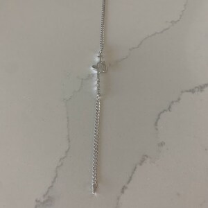 Puede incluir: Un brazalete de cadena de plata con un peque&ntilde;o dije de plata en forma de cruz.