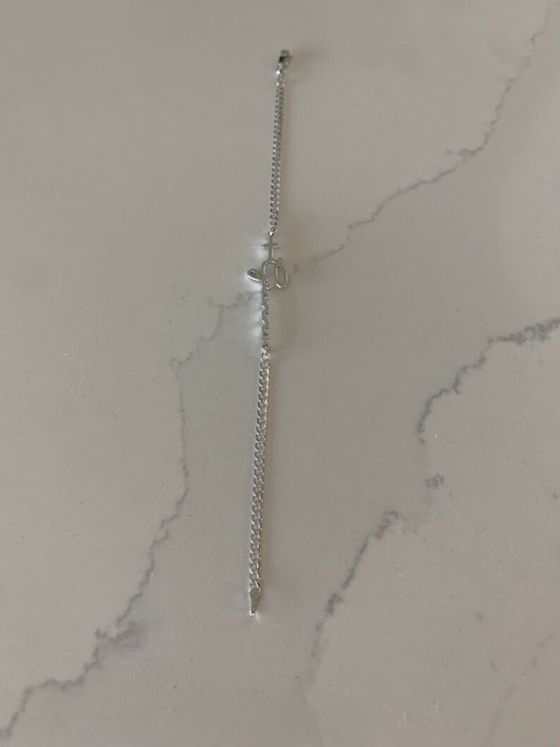 Puede incluir: Un brazalete de cadena de plata con un peque&ntilde;o dije de plata en forma de cruz.