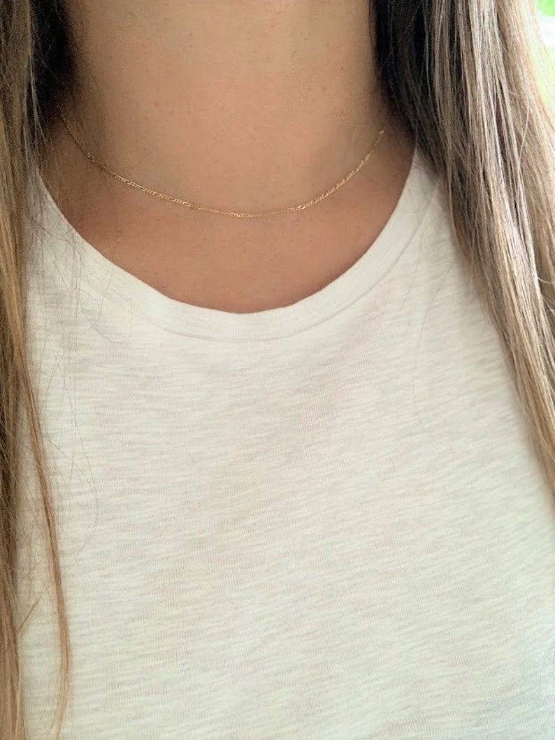 May include: A delicate gold chain necklace, worn by a person, with a simple design.
