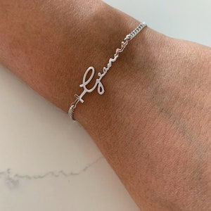 Puede incluir: Una pulsera de plata con una cadena delicada y un dije de nombre en escritura cursiva que dice "Gian".
