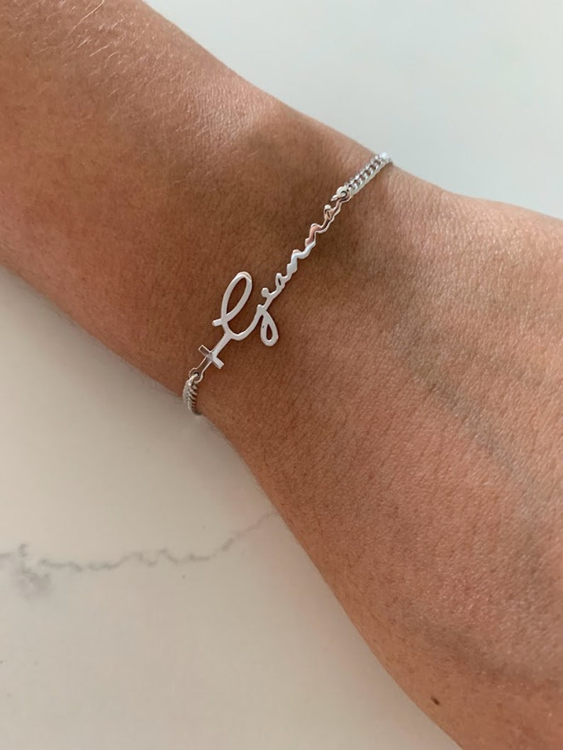 Puede incluir: Una pulsera de plata con una cadena delicada y un dije de nombre en escritura cursiva que dice "Gian".