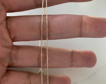 Può includere: Due catene d'oro, una leggermente più lunga dell'altra, sono tenute in una mano. Le catene sono delicate e hanno un design semplice.