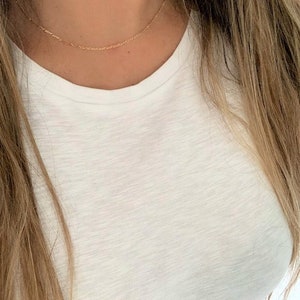 May include: A delicate gold chain necklace worn on a person's neck. The chain is thin and has a simple design.