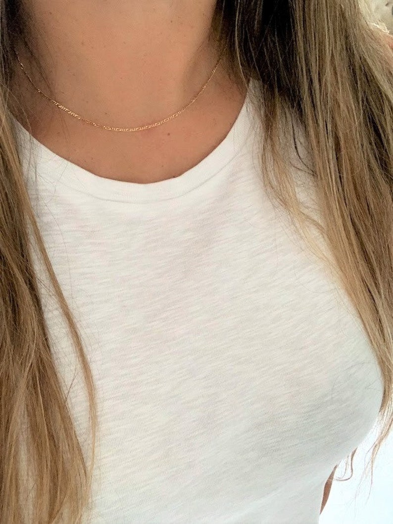 May include: A delicate gold chain necklace worn on a person's neck. The chain is thin and has a simple design.