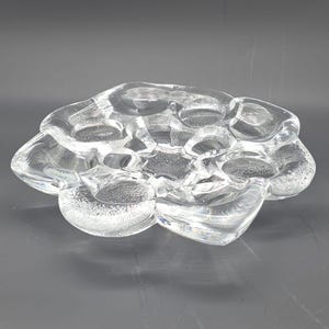 Peut inclure: Un bol décoratif en verre transparent avec une forme organique unique. Le bol présente une série de compartiments arrondis interconnectés, créant une surface texturée. Le verre est transparent, laissant passer la lumière.