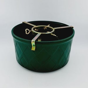 May include: A dark green Christmas tree stand with a diamond pattern on the exterior. The stand has a gold-coloured metal tree holder. The stand is designed to hold a Christmas tree upright.