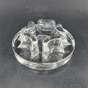 Puede incluir: Un jarrón de flores de vidrio transparente con una base circular y cinco aberturas para tallos de flores.