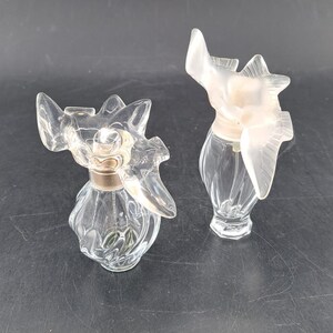 May include: Two clear glass perfume bottles with a bird design. The bottles have a textured surface and a gold-coloured cap.