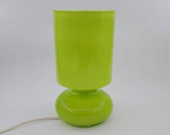 May include: A bright green glass table lamp with a cylindrical shade and a rounded base.