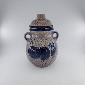 May include: A ceramic jar with a lid, featuring a textured, speckled beige surface. The jar has a dark blue band around the top and is adorned with dark blue fruit illustrations. It has two small handles and the word "Rumor" is written on the jar.