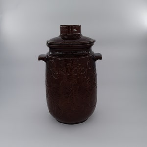 May include: A brown ceramic jar with a lid, decorated with cherries and the word "Rumtopf".