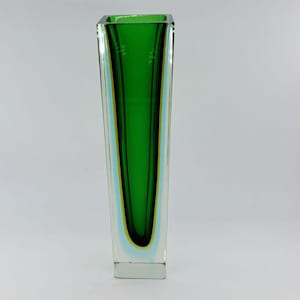 Könnte beinhalten: Eine hohe, rechteckige Glasvase mit leuchtend grünem Innenraum und klarer Außenseite. Die Vase hat ein modernes, minimalistisches Design, perfekt für die Präsentation von Blumen oder als dekoratives Element. Die Vase ist etwa 25 cm hoch.