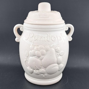 May include: White ceramic jar with a lid and two handles. The jar has a raised design of fruit and the word "Tomato" on the front.