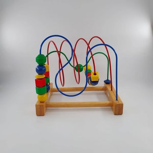 Pode incluir: Um brinquedo de madeira com contas coloridas e um labirinto de laços de arame. O brinquedo é projetado para crianças aprenderem sobre cores e formas.