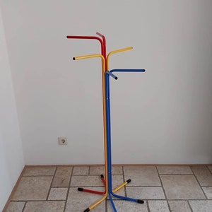 May include: A colorful metal coat rack with four arms. The rack is made of red, yellow, and blue metal and has a star-shaped base.