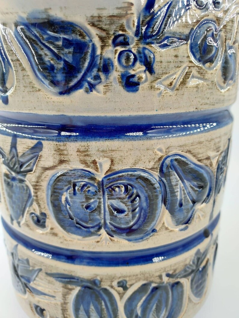 Peut inclure: Un vase en c&eacute;ramique blanche avec des motifs floraux bleus. Le vase a une surface textur&eacute;e et est d&eacute;cor&eacute; de fleurs, de feuilles et de baies bleues.