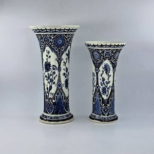 Może przedstawiać: Dwa niebiesko-białe wazony ceramiczne z misternymi wzorami kwiatowymi. Wyższy wazon jest nieco szerszy u góry i ma bardziej wyraźne rozszerzenie.