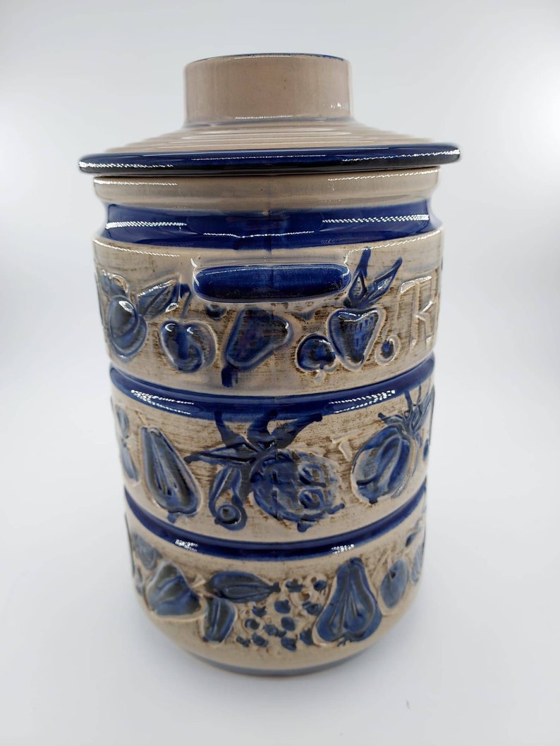 Peut inclure: Un pot en c&eacute;ramique avec un motif bleu et blanc repr&eacute;sentant une vari&eacute;t&eacute; de fruits. Le pot a un couvercle et une poign&eacute;e.