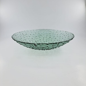 Puede incluir: Un cuenco grande, redondo, de vidrio verde con una superficie texturizada. El cuenco tiene un borde ligeramente elevado y es perfecto para servir aperitivos o fruta.