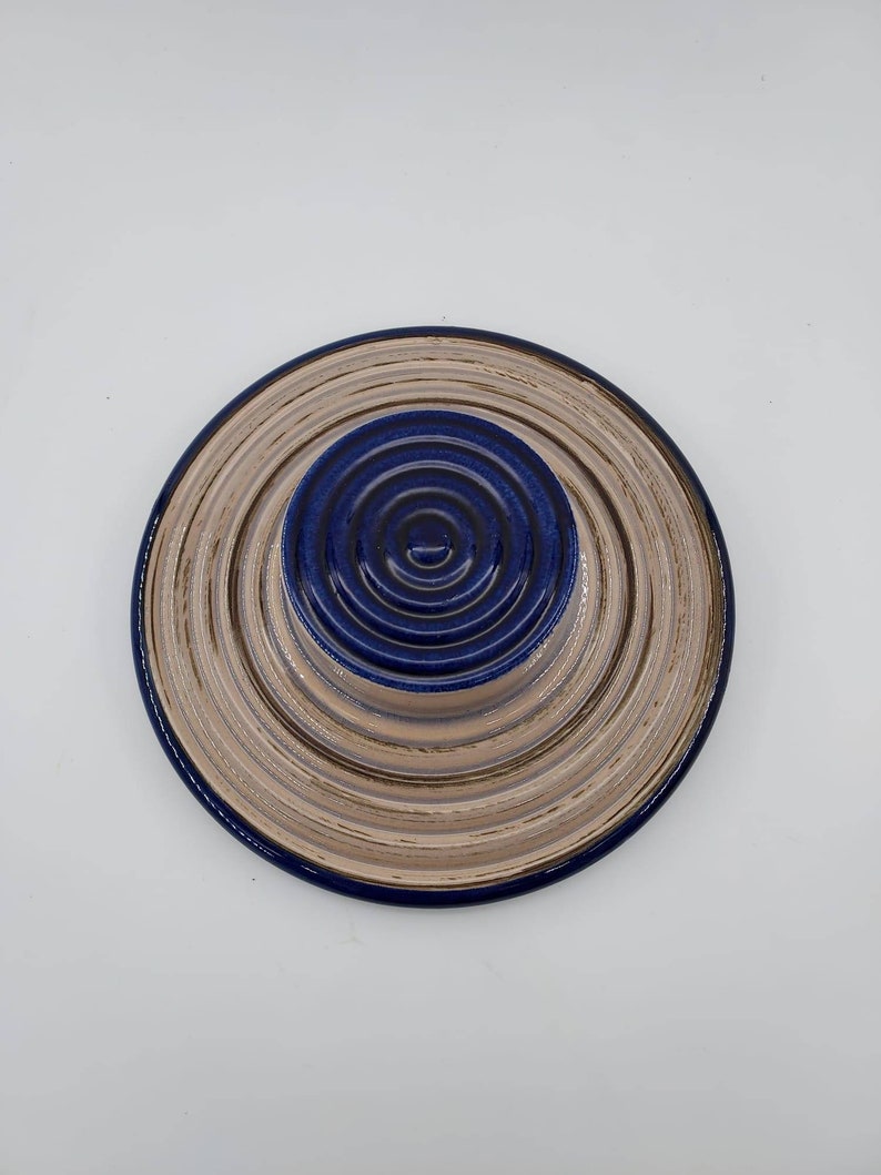 Peut inclure: Une assiette en c&eacute;ramique avec des cercles concentriques dans des tons beige et bleu. L'assiette a un centre sur&eacute;lev&eacute; avec un motif de cercle bleu.