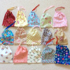 May include: A collection of fifteen small fabric drawstring pouches arranged in three rows. Each pouch features a unique pattern, including floral, polka dot, and star prints in various colours such as red, yellow, blue, pink, and green.