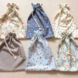May include: Six fabric drawstring pouches featuring various floral patterns. The bags include designs with light green, blue, cream, grey, and light blue backgrounds, each finished with a simple white cord closure at the top for securing contents.