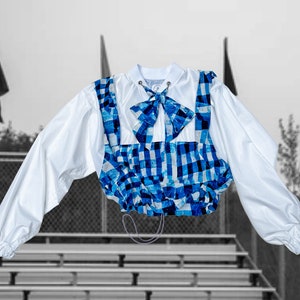 May include: A white cropped jacket with a blue and white checkered pattern. The jacket has a bow tie and a drawstring closure.