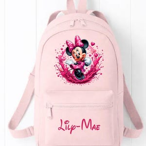 May include: A light pink backpack featuring a graphic of Minnie Mouse surrounded by pink paint splashes and small hearts. The front pocket displays the name Lily-Mae in a dark pink script font. The bag has adjustable shoulder straps and a top handle.