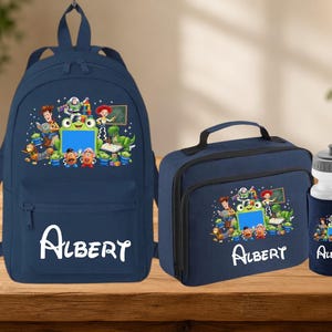May include: A navy blue backpack, lunch bag, and water bottle set featuring Toy Story character graphics and the name Albert in white text. The backpack has a large main compartment and front pocket, while the lunch bag is rectangular with a handle.