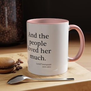 May include: White ceramic mug with a pink rim and handle. The mug features a black quote that reads "And the people loved her much."  The quote is attributed to Lord Tennyson, 1809-1892.