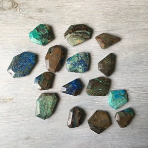 May include: A collection of 14 irregularly shaped, faceted, green and brown gemstone cabochons. The stones have a mottled, marbled appearance with shades of blue, green, and brown.