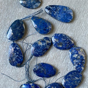 Puede incluir: Una hebra de diez cuentas de piedra preciosa de lapislázuli azul y blanco, cada una con un patrón y una forma únicos, enhebradas en un hilo negro.