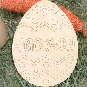 May include: A wooden Easter egg shaped ornament with a chevron pattern and polka dots. The name "JACKSON" is written in a whimsical font on the egg.