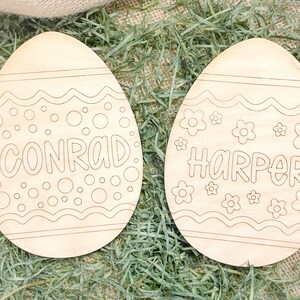 May include: Two unfinished wooden Easter eggs with a decorative design. One egg has the name Conrad and the other has the name Harper.