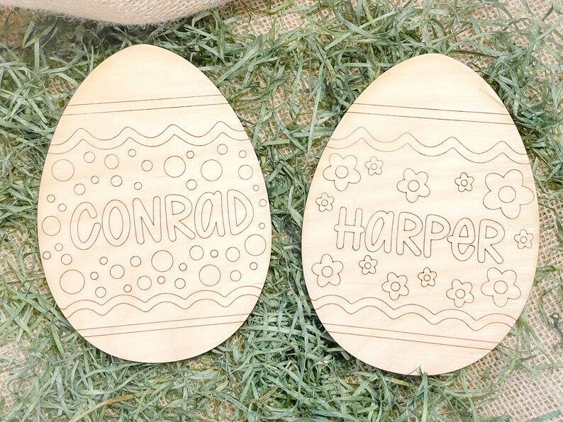 May include: Two unfinished wooden Easter eggs with a decorative design. One egg has the name Conrad and the other has the name Harper.