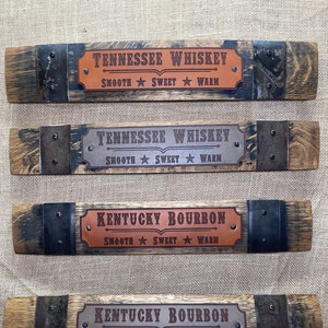 May include: Four wooden barrel stave signs with metal accents. The signs feature leather labels with the text "Tennessee Whiskey Smooth Sweet Warm" and "Kentucky Bourbon Smooth Sweet Warm".