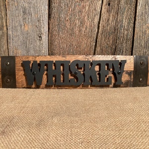 May include: A wooden sign with the word "WHISKEY" in black metal letters. The sign is made from reclaimed wood and has metal accents.