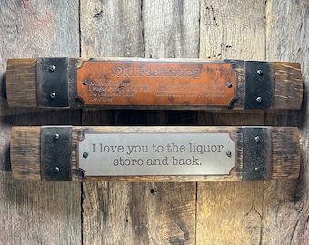 May include: Two wooden signs with metal accents hanging on a wood wall. The top sign has a brown leather plaque with the text "Old Fashioned" and the recipe for the cocktail. The bottom sign has a silver plaque with the text "I love you to the liquor store and back."
