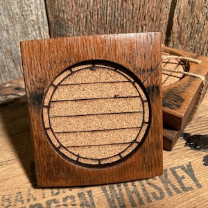 May include: Four square wooden coasters with a round cork insert. The coasters are made from reclaimed whiskey barrels and have a rustic brown color.
