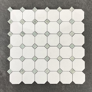 May include: White and gray octagonal tile mosaic with diamond-shaped accents. The mosaic features a repeating pattern of white octagons connected by small gray diamond tiles, creating a geometric design. The tiles are arranged on a dark gray surface.
