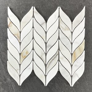 May include: White and beige marble leaf-shaped mosaic tile arranged in a repeating pattern. The tiles are set on a black mesh backing. The mosaic features veining and subtle color variations, creating a natural stone look. Ideal for backsplashes or accent walls.