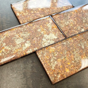 May include: Close-up of a set of brown and gold mosaic tiles with a glossy finish. The tiles are arranged in a staggered pattern.