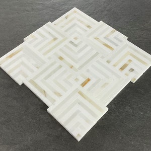 May include: White marble tile with a geometric pattern of intersecting lines. The tile has a subtle, light brown color variation.