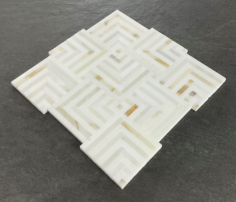 May include: White marble tile with a geometric pattern of intersecting lines. The tile has a subtle, light brown color variation.