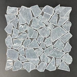 May include: A sheet of gray stone mosaic tiles arranged in a random pattern on a mesh backing. The tiles are irregular in shape and size, and have a slightly textured surface.