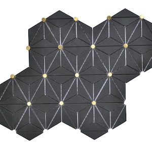 May include: Geometric black tile mosaic with gold-colored accents. The tiles are hexagonal and feature a repeating triangular pattern. The gold accents are small, circular, and evenly spaced across the surface. The design is modern and visually striking.